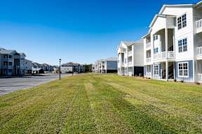 A row of white apartment buildings with a grassy field in front.