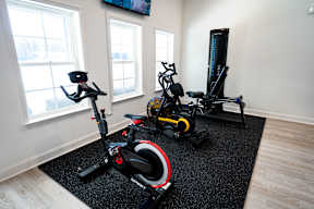 A room with a black exercise bike, a black and red stationary bike, and a black and yellow stationary bike.