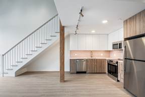 A modern kitchen with stainless steel appliances and a wooden staircase.