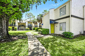 A white building with a yellow door is surrounded by greenery.