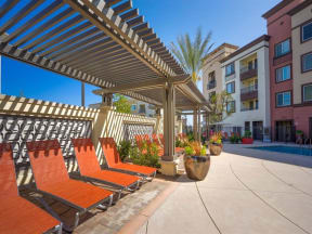 a pergola with orange lounge chairs and potted plants in front of an apartment building