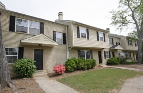 the front of a tan house with black shutters and a lawn and a sidewalk