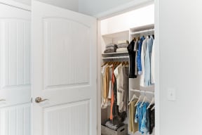 a closet with a white door and clothes hanging in it