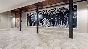 A black and white mural of people in suits is on the wall of a room with tiled floors and wooden beams.