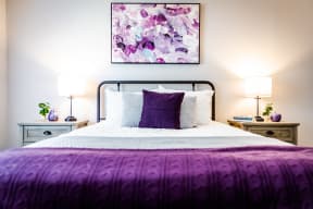 a bedroom with a bed with a purple blanket and white bedding
