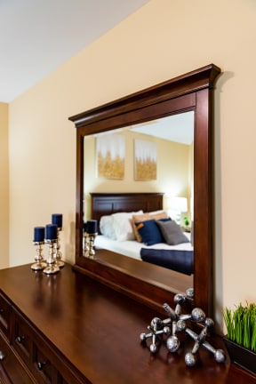 a bedroom with a large mirror and a wooden dresser with a bed in the reflection