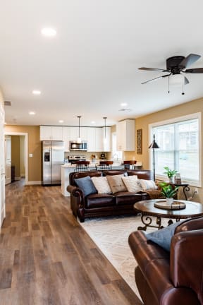 a living room with brown leather couches and a kitchen with white cabinets and stainless steel appliances