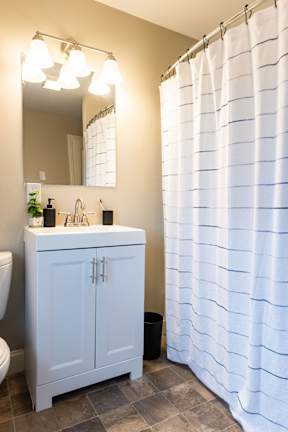 A white bathroom with a sink, mirror, and shower curtain.