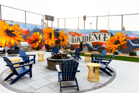 a patio with blue chairs and yellow tables and a fire pit