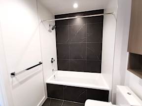 A white bathroom with black tiles and a white bathtub.