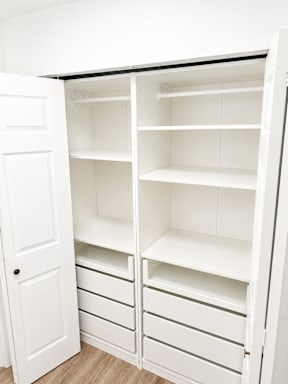 A white pantry with shelves and drawers is open.