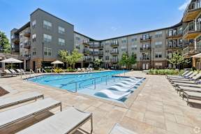 A large swimming pool surrounded by sun loungers and apartment buildings.