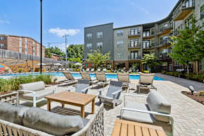 A poolside area with chairs and tables in front of apartment buildings.