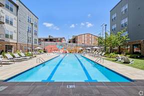 A large outdoor swimming pool surrounded by lounge chairs and buildings.