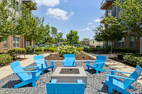 A sunny day at a park with blue chairs and a fire pit.