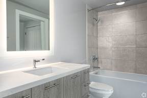 Dark finish cabinetry in  a bathroom with baklit mirror, sink, toilet and shower
