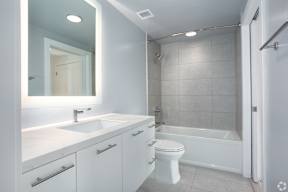 Secondary bathroom with backlit mirrors and shower with bathtub