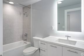 a white bathroom with a backlit mirror and a toilet and a tub