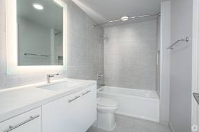a white bathroom with a backlit mirror and a toilet and a tub