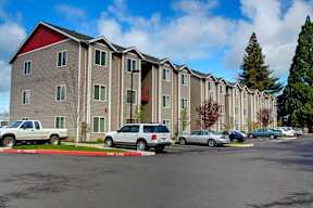 A row of apartment buildings with cars parked in front.
