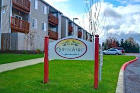 A sign for Queen Anne apartments stands in front of a building.