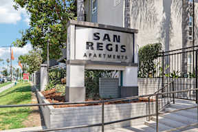 A sign for San Regis Apartments is displayed in front of a building.