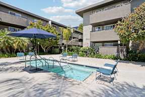 A pool area with a blue umbrella and chairs.
