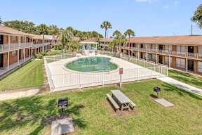 A pool surrounded by a fence and benches in front of apartment buildings.