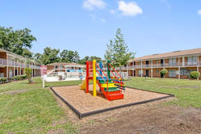 A playground with a slide and a sandbox in the middle of a grassy area.