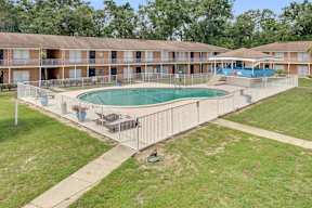 A swimming pool is surrounded by a fence and chairs in front of apartment buildings.