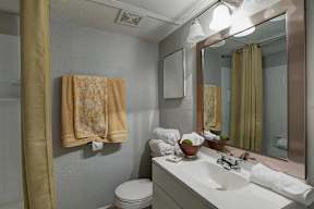 A bathroom with a toilet, sink, mirror, and a towel hanging on the wall.