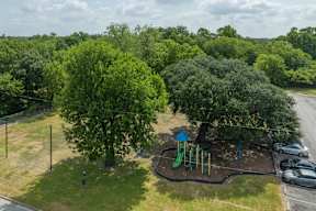 A playground with a green slide and a blue umbrella is surrounded by trees.