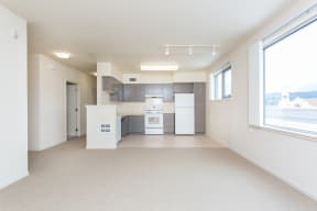 an empty living room with a kitchen and a window