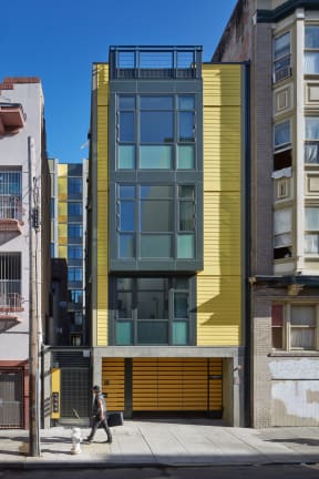 a narrow building with a yellow and green facade and a sidewalk