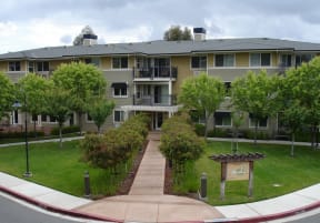 an exterior view of an apartment building with a green lawn and trees