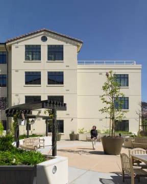 a man walking in front of a white building with tables and plants