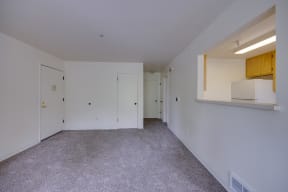 the living room and kitchen of an apartment with white walls and carpet
