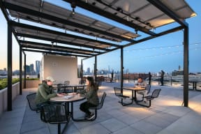 people sitting at tables on a rooftop terrace with a city skyline