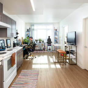 a living room and kitchen with a person sitting at a desk