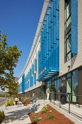 a building with blue shutters on the facade and people walking down a sidewalk