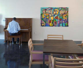 a man playing a piano in a room with a table and chairs