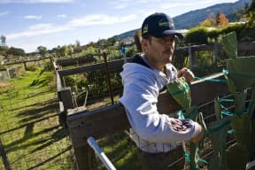 a man standing next to a fence holding a watering can