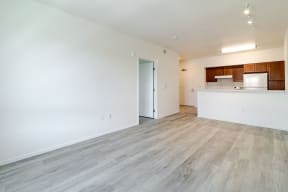the living room and kitchen of an apartment with white walls and wood flooring