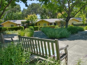 a park bench on a sidewalk in front of a yellow house