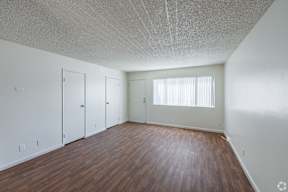 A room with wooden floors, a window, and three doors.