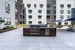 A BBQ grill is in the middle of a courtyard surrounded by buildings.
