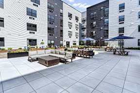 A large patio area with tables and chairs is surrounded by modern apartment buildings.