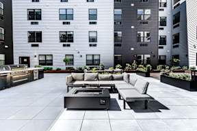A modern outdoor seating area with a fireplace in front of a tall building.