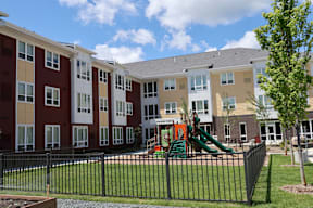 A playground with a green slide is in front of a building.
