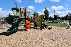 A playground with a green slide and orange and green play structures.